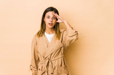 Bej arka planda izole edilmiş genç bir kadın. Uzağa bakıyor. Elini alnına koyuyor..