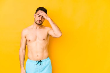 Sarı arka planda mayosu olan genç beyaz adam şakaklarına dokunan ve baş ağrısı çeken beyaz bir adam..