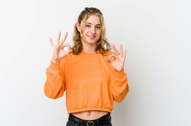 Beyaz arka plandaki genç beyaz kadın neşeli ve kendinden emin, iyi bir jest yapıyor..