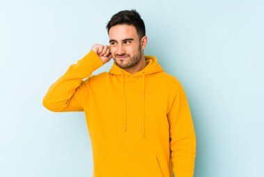 Genç beyaz adam mavi arka planda izole edilmiş parmaklarıyla kulaklarını kapatıyor, gürültülü bir ortam tarafından stresli ve umutsuz..