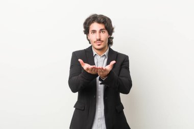 Beyaz arka planda genç bir iş adamı elinde avuç içi bir şeyle kameraya sunuyor..