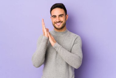 Mor arka planda izole olmuş genç beyaz adam enerjik ve rahat hissediyor, ellerini ovuşturuyor..