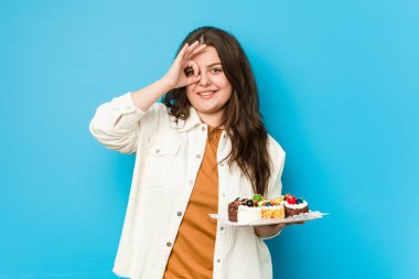 Genç, kıvrımlı bir kadın elinde tatlı bir pasta tutuyor..