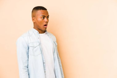 Genç Latin bir adam bej arka planda izole edilmiş. Gördüğü bir şey yüzünden şok oluyor..