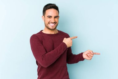 Mavi arka planda izole edilmiş genç beyaz adam işaret parmağıyla fotokopi alanını işaret ederek heyecan ve arzusunu ifade ediyor..