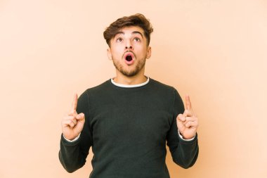 Bej arka planda izole edilmiş genç bir Arap adam ağzı açık bir şekilde üst tarafı işaret ediyor..