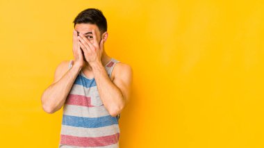 Kafkasyalı genç adam sarı bir alanda izole edilmiş parmaklarıyla gözünü kırp korkmuş ve gergin..