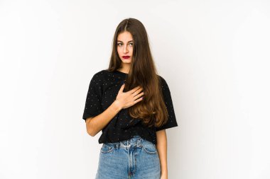 Beyaz arka planda izole edilmiş genç beyaz kadın yemin ediyor, elini göğsüne koyuyor..