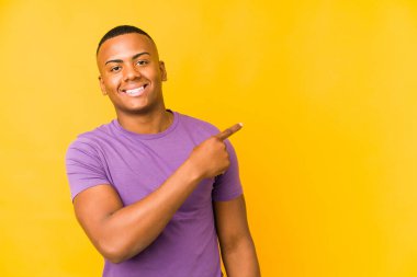 Sarı arka planda izole edilmiş genç latin adam gülümsüyor ve boş alanda bir şeyler gösteriyor..