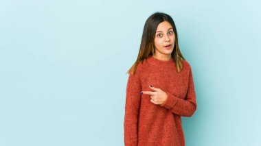 Mavi arka planda izole edilmiş genç bir kadın gülümsüyor ve boş alanda bir şeyler gösteriyor..