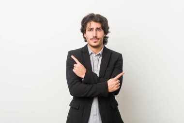 Genç bir iş adamı beyaz arka planda iki seçenek arasında seçim yapmaya çalışıyor..