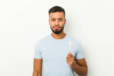 Elinde diş fırçası tutan Güney Asyalı genç adam kafası karışmış, kuşkulu ve kararsız hissediyor..