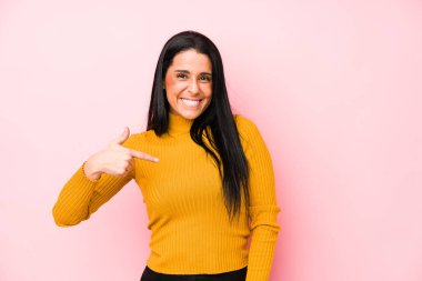 Pembe arka planda izole edilmiş genç beyaz bir kadın gömlek fotokopi odasını işaret ediyor, gururlu ve kendinden emin.