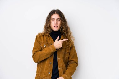 Uzun saçlı adam yalnız poz veriyor. Gülümsüyor ve işaret ediyor. Boş alanda bir şey gösteriyor..