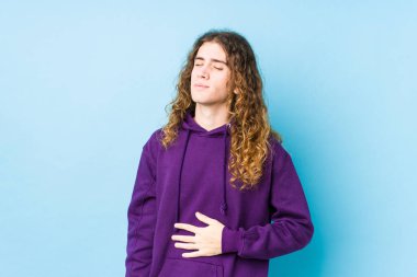 Uzun saçlı yalnız poz veren adam karnına dokunur, nazikçe gülümser, yemek yer ve tatmin olur..