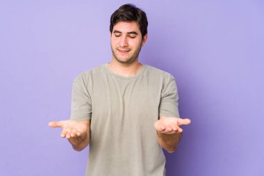 Mor arka planda izole edilmiş genç bir adam elinde avuç içi bir şeyle kameraya sunuyor..
