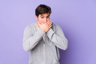 Mor arka planda izole edilmiş genç bir adam ağzını kapatıyor ve elleri endişeli görünüyor..