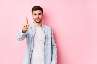 Beyaz arka planda poz veren Kafkasyalı genç iş adamı bir numarayı parmağıyla gösteriyor.
