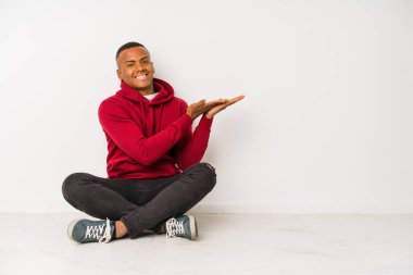 Yerde tek başına oturan genç Latin bir adam. Elinde palmiyenin üzerinde bir kopyası var..