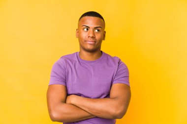 Sarı arka planda izole edilmiş genç latin adam alaycı bir ifadeyle kameraya bakıyor..