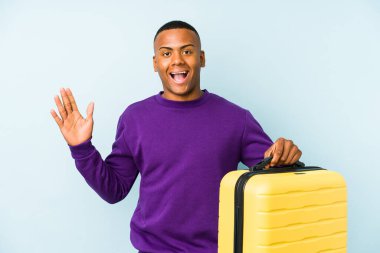 Elinde bavul tutan genç bir gezgin hoş bir sürpriz bekliyor, heyecanlı ve el kaldırıyor..