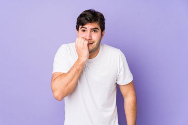 Mor arka planda izole edilmiş, tırnak yiyen, gergin ve endişeli genç bir adam..