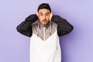 Kafkasyalı genç adam mor arka planda izole edilmiş kulakları kulaklarıyla kapatıyor çok fazla ses duymamaya çalışıyor..