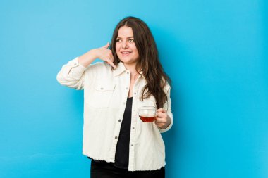 Elinde çay fincanı tutan, cep telefonu hareketini parmaklarıyla gösteren kıvrımlı bir kadın..