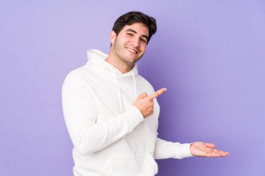 Mor arka planda izole edilmiş genç bir adam heyecanlı bir şekilde avuç içinin bir kopyasını tutuyor..