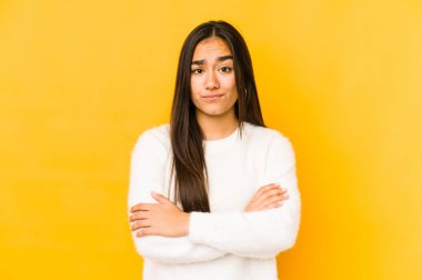 Sarı arka planda izole edilmiş genç bir kadın kameraya alaycı bir ifadeyle bakıyor..