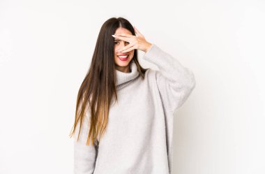 Beyaz arka planda izole edilmiş beyaz tenli genç bir kadın kameraya parmaklarıyla göz kırpıyor, yüzünü kapatmaktan utanıyor..