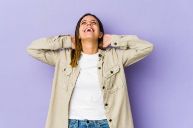 Mor arka planda izole edilmiş genç bir kadın kendini güvende hissediyor, elleri başının arkasında..