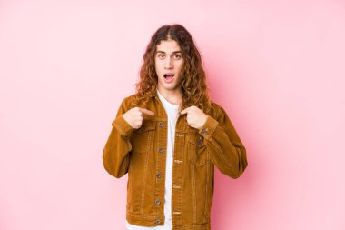 Genç, uzun saçlı, yalnız poz veren, şaşkın, parmağıyla işaret eden, geniş bir gülümseme..