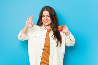 Genç kıvrımlı kadın elinde kurabiyelerle neşeli ve kendinden emin, iyi bir jest yapıyor..