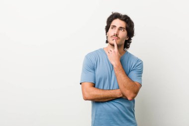 Beyaz bir arka planı olan genç ve yakışıklı bir adam şüpheli ve şüpheci bir ifadeyle yana bakıyor..