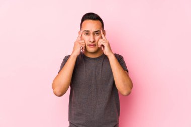 Pembe arka planda poz veren yog latin adam bir göreve odaklanmış, işaret parmaklarını işaret ediyor..