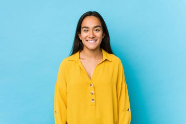 Genç Hintli bir kadın, mavi üzerine izole bir şekilde gülümsüyor