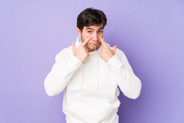 Mor arka planda izole edilmiş genç bir adam ağlıyor, bir şeyden memnun değil, acı ve kafa karışıklığı konsepti..