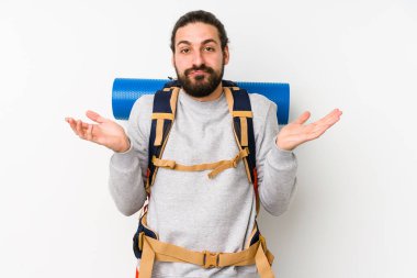 Sırt çantalı genç adam beyaz bir arka planda izole edilmiş. Sorgulama sırasında omuz silkiyor ve şüphe ediyor..