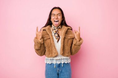 Koyun derisi ceketli genç Hintli kadın parmaklarıyla kaya jesti yapıyor.