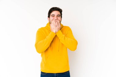 Beyaz arka planda izole edilmiş genç bir adam bir şeye gülüyor, elleriyle ağzını kapatıyor..
