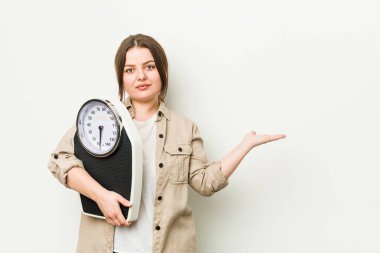 Avuç içlerindeki fotokopi alanını gösteren bir terazi tutan ve elini beline koyan genç ve kıvrımlı kadın..
