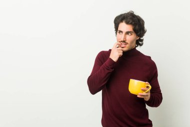 Kafkasyalı genç bir adam elinde kahve fincanıyla rahatlamış fotokopi odasına bakan bir şey düşünüyor..