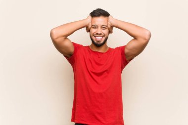 Genç Güney Asyalı adam ellerini başının üstünde tutarak neşeyle gülüyor. Mutluluk kavramı.