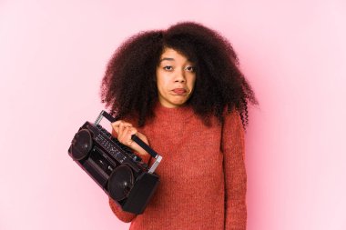 Elinde kaset tutan genç bir afro kadın omuz silkiyor ve gözleri açık..