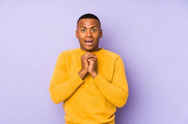 Mor arka planda izole edilmiş genç Latin adam şans için dua ediyor, şaşırmış ve ağzını açıyor..