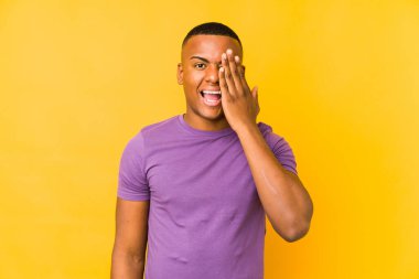 Sarı arka planda izole edilmiş genç latin adam yüzünün yarısını palmiye ile kaplayarak eğleniyor..