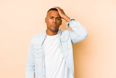 Genç latin adam bej arka planda izole edilmiş. Çok yorgun ve uykulu. Elini başının üstünde tutuyor..