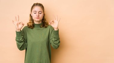 Beyaz tenli genç bir kadın, bej arka planda izole edilmiş yoğun çalışma gününden sonra rahatlıyor, yoga yapıyor..