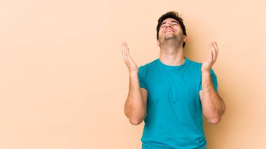 Bej arka planda izole edilmiş genç bir adam neşeli bir şekilde gülüyor. Mutluluk kavramı.